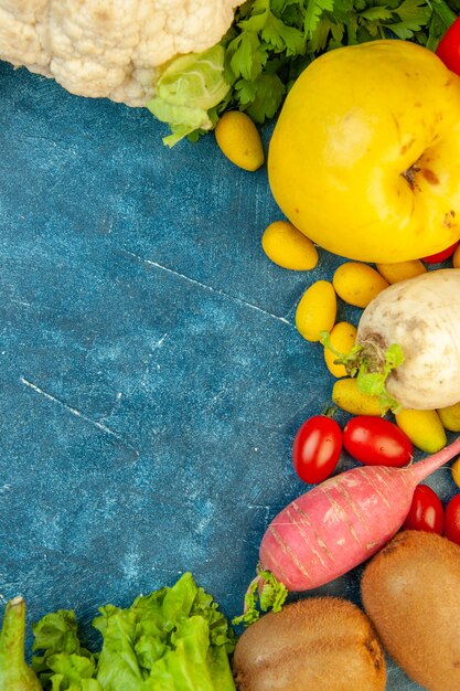 Vista superior de verduras frescas pimientos membrillo cumcuats coliflor kiwi sobre fondo azul.