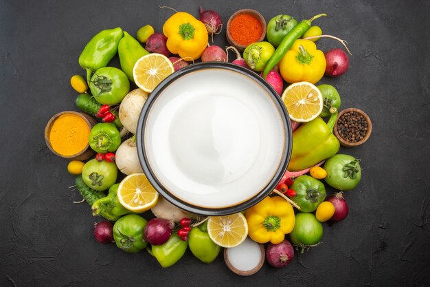 Vista superior de verduras frescas con plato vacío sobre un fondo oscuro