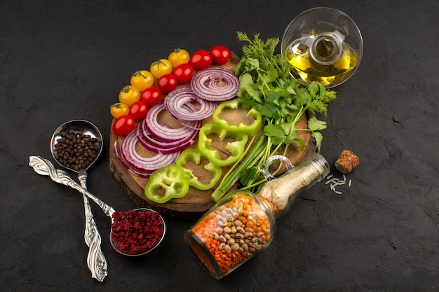 vista superior verduras frescas en rodajas coloridas y enteras, como cebollas en rodajas pimientos verdes tomates amarillos y rojos en el escritorio marrón y oscuro