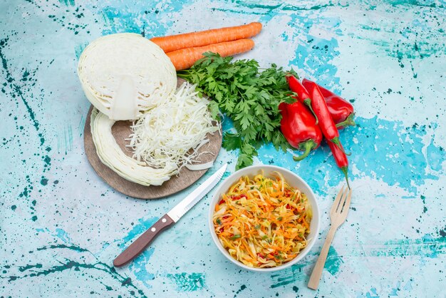 Vista superior de verduras frescas en rodajas Ensalada de piezas largas y delgadas dentro del plato con verduras, repollo, pimientos en la superficie azul brillante, comida, almuerzo, vegetales, ensalada saludable