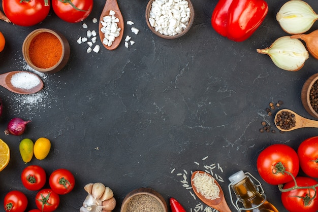 Vista superior de verduras frescas, sal, pimienta negra, arroz en cucharas de madera, tomates, especias en tazones pequeños, pimientos, cumcuats en la mesa negra, lugar de copia en el centro