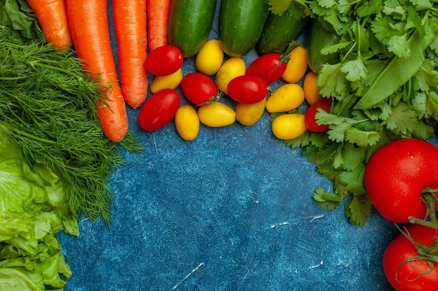 Vista superior de verduras frescas tomate perejil lechuga eneldo zanahoria pepino cumcuat tomates cherry sobre fondo azul.