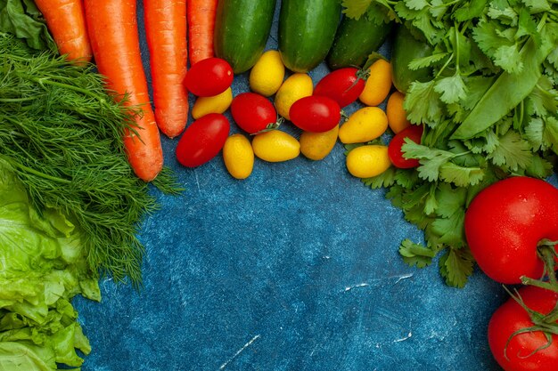 Vista superior de verduras frescas tomate perejil lechuga eneldo zanahoria pepino cumcuat tomates cherry sobre fondo azul.