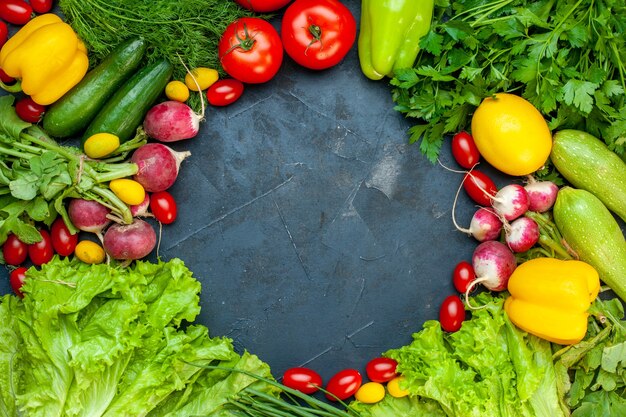 Vista superior de verduras frescas tomates lechuga rábano limón calabacín perejil tomates cherry en la superficie oscura espacio libre en el centro