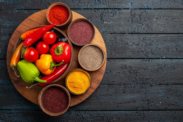 Vista superior de verduras frescas tomates y pimiento con condimentos en el escritorio oscuro