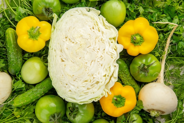 Vista superior de verduras frescas con tomates verdes, rábano y pimientos sobre fondo blanco.
