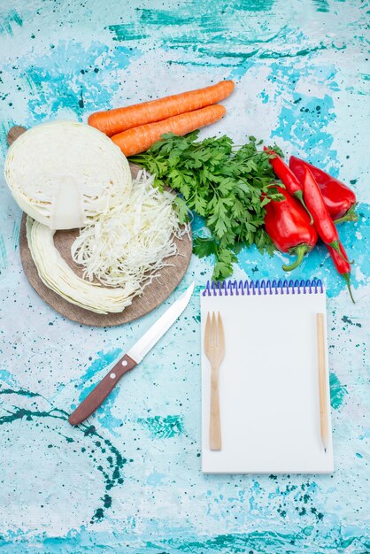 Vista superior de verduras frescas, verduras, repollo en rodajas, zanahorias y pimientos con bloc de notas en azul brillante, comida, comida, verduras, almuerzo, ensalada saludable