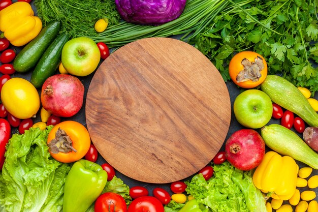 Vista superior de verduras y frutas, lechuga, tomates, pepino, eneldo, tomates cherry, calabacín, cebolla verde, perejil, granada, caqui, manzana, tablero de madera redonda en el centro