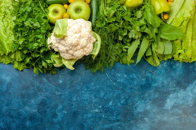 Vista superior de verduras y frutas pepino perejil eneldo pimientos lechuga manzanas coliflor sobre fondo azul.