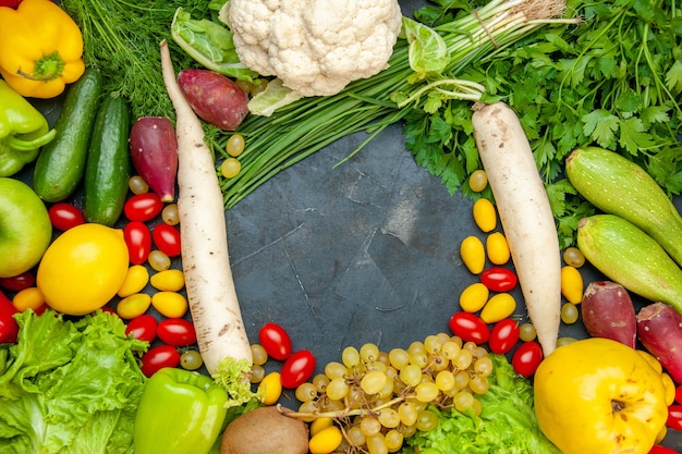 Vista superior de verduras y frutas, tomates cherry, lechuga cumcuat, membrillo, uva, limón, coliflor, rábano blanco, perejil, calabacín, pepinos, espacio libre en el centro
