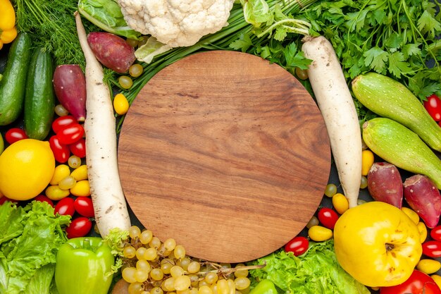 Vista superior de verduras y frutas tomates cherry lechuga cumcuat membrillo uva limón coliflor rábano blanco perejil calabacín pepinos tablero de madera redonda en el centro