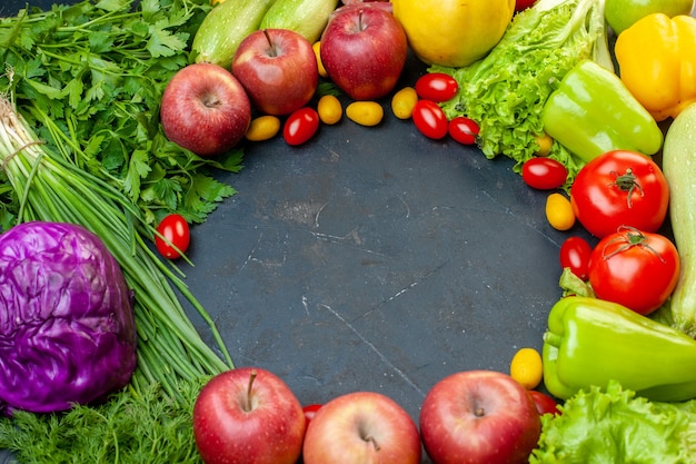 Vista superior de verduras y frutas, tomates cherry, manzanas cumcuat, repollo morado, cebolla verde, lechuga, perejil, pimientos con lugar libre