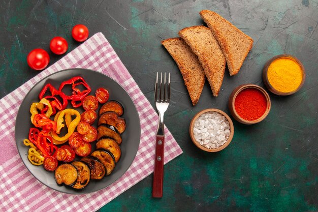 Vista superior de verduras en rodajas cocidas, pimientos y berenjenas con condimentos y pan sobre superficie verde