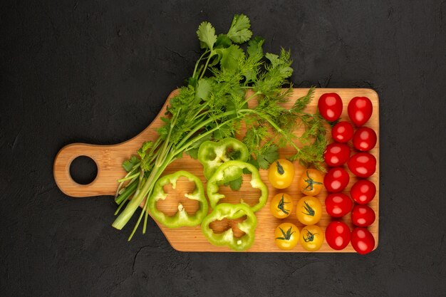 Vista superior de verduras en rodajas y enteras como pimiento verde amarillo tomate rojo sobre el fondo oscuro