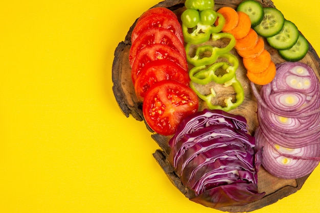 Foto gratuita vista superior de verduras en rodajas repollo rojo cebolla tomates pimientos zanahoria y pepinos en una tabla de madera en amarillo j