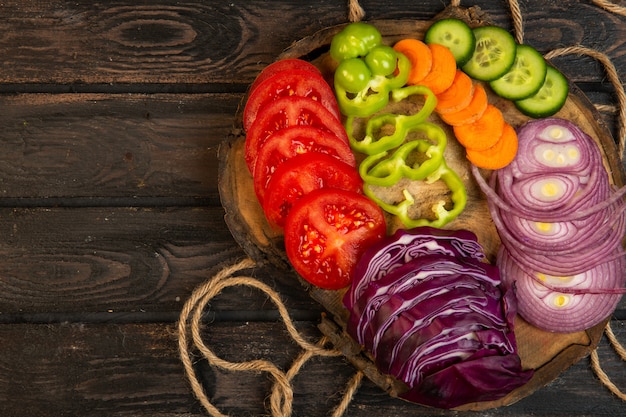 Foto gratuita vista superior de verduras en rodajas repollo rojo cebolla tomates pimientos zanahoria y pepinos en una tabla de madera j