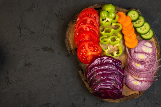 Vista superior de verduras en rodajas repollo rojo cebolla tomates pimientos zanahoria y pepinos en una tabla de madera sobre negro