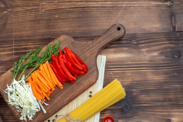 Vista superior de verduras en rodajas, repollo, zanahoria y pimiento en la superficie marrón de la tabla de cortar