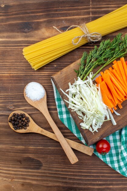 Vista superior de verduras en rodajas, repollo, zanahoria y pimiento en la superficie marrón de la tabla de cortar