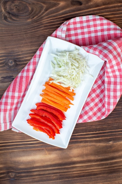 Foto gratuita vista superior de verduras en rodajas, zanahoria, pimientos y repollo sobre superficie marrón