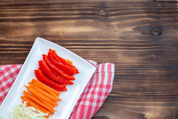 Vista superior de verduras en rodajas, zanahoria, pimientos y repollo sobre superficie marrón