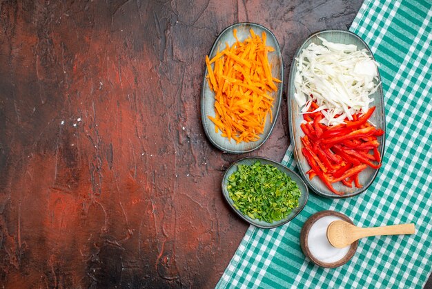 Vista superior de verduras en rodajas, zanahoria, repollo y pimiento con verduras en la mesa oscura
