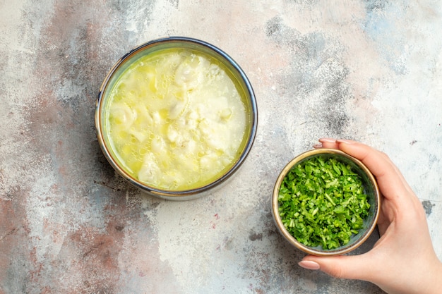 Vista superior de verduras de sopa de albóndigas dushbara en un tazón en la mano femenina sobre una superficie desnuda con espacio de copia