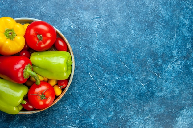 Vista superior de verduras tomates cherry cumcuat pimientos tomates de diferentes colores en un plato de madera en la mesa azul con espacio libre