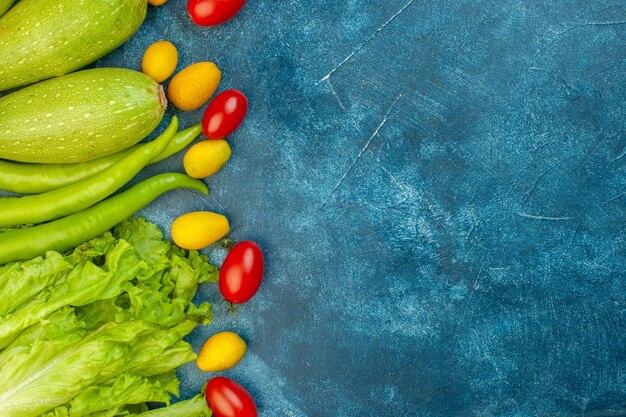 Vista superior de verduras tomates cherry zacchini cumcuat pimientos verdes lechuga en mesa azul