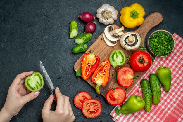 Vista superior de verduras tomates pimientos en tabla de cortar verduras en un tazón pepinos sobre mantel rojo
