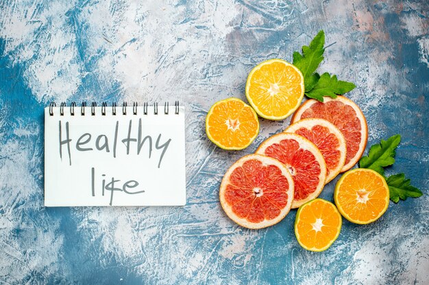 Vista superior vida sana escrita en el bloc de notas cortadas naranjas y pomelos en superficie blanca azul