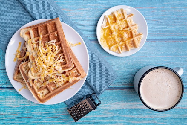 Vista superior de waffles en placa con queso rallado y bebidas