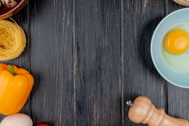 Vista superior de la yema de huevo y la clara en un recipiente con un pimiento naranja sobre un fondo de madera con espacio de copia