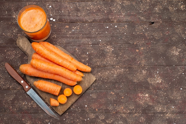 Vista superior de zanahorias anaranjadas en rodajas y enteras con jugo de zanahoria fresco en marrón