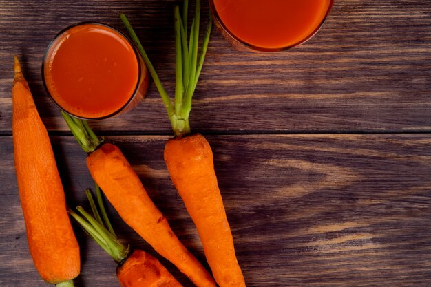 Vista superior de zanahorias enteras con jugo de zanahoria sobre fondo de madera con espacio de copia