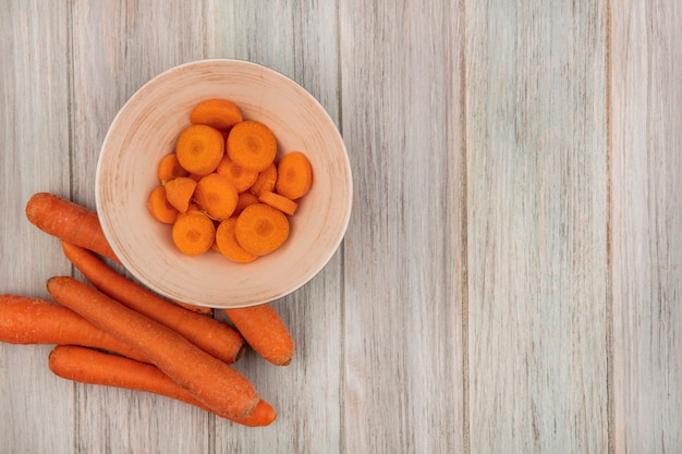 Vista superior de zanahorias picadas de naranja en un recipiente con zanahorias aislado sobre una superficie de madera gris con espacio de copia