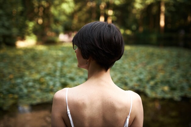 Vista trasera al aire libre de la joven morena con corte de pelo corto admirando la hermosa naturaleza salvaje