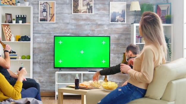 Foto gratuita vista trasera de amigos bebiendo cerveza y viendo deportes en la televisión con pantalla verde en la sala de estar.