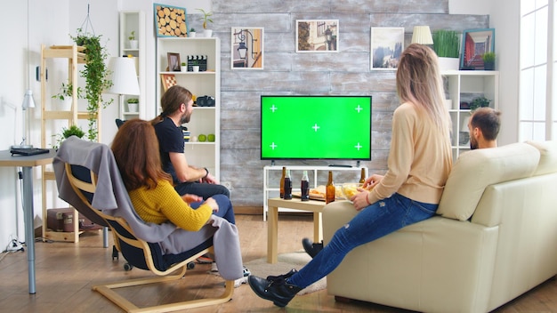 Vista trasera de amigos cercanos con las manos en el aire mientras ven un partido de fútbol en la sala de estar.