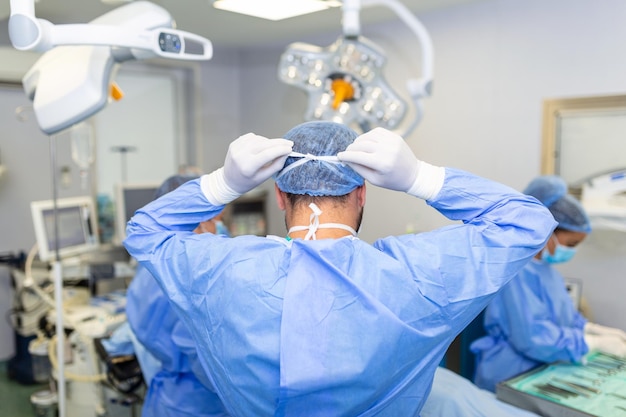 Foto gratuita vista trasera del cirujano masculino con mascarilla quirúrgica en el quirófano del hospital