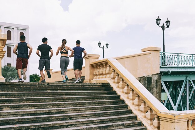 Vista trasera de cuatro personas en ropa deportiva corriendo arriba en el centro de la ciudad