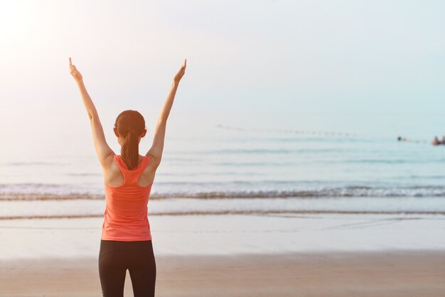 Vista trasera de deportista estirando sus brazos en la playa