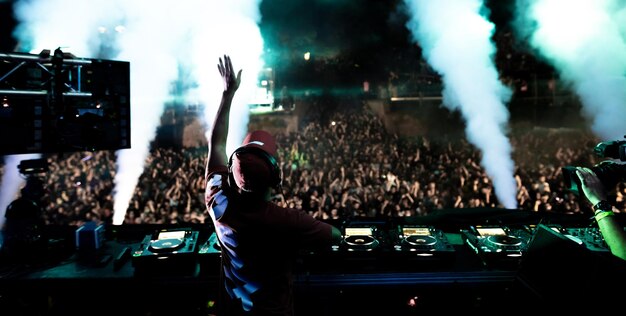 Vista trasera de un DJ tocando música frente a una multitud emocionada en el festival de música por la noche