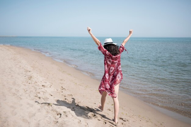 Vista trasera emocionada mujer caminando a la orilla del mar