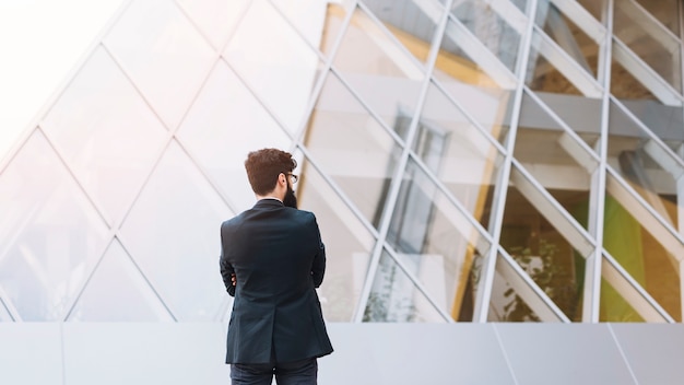 Vista trasera del empresario de pie frente al moderno edificio corporativo