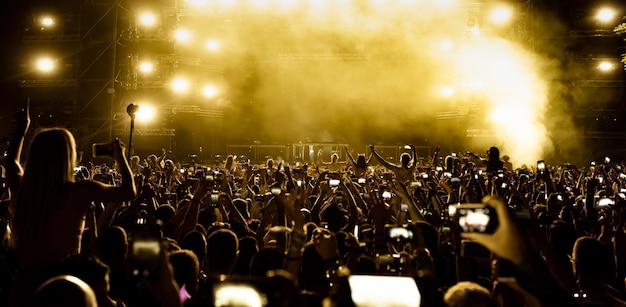 Vista trasera de fanáticos emocionados divirtiéndose en el festival de música y tomando fotos del escenario con sus teléfonos inteligentes Copiar espacio