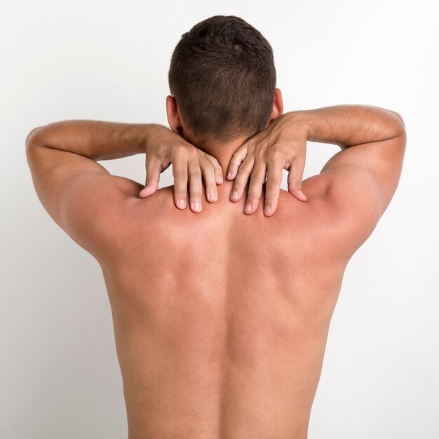 Vista trasera del hombre sin camisa con dolor de espalda de pie contra la pared blanca