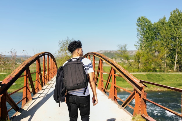 Vista trasera del hombre joven que camina en el puente sobre el río hermoso