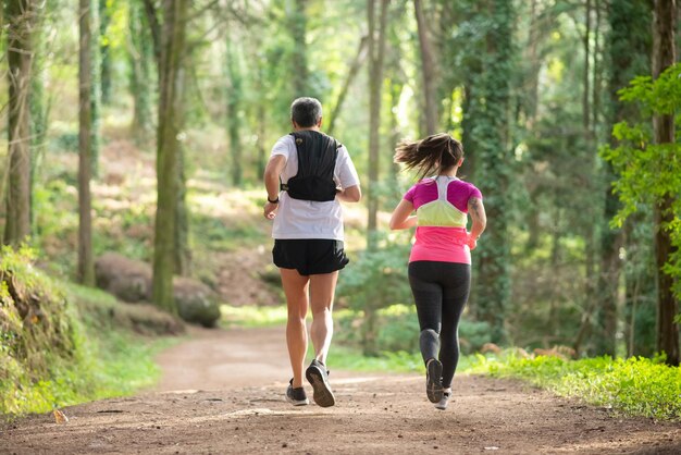 Vista trasera de un hombre y una mujer enérgicos trotando en el bosque. Dos deportistas con ropa deportiva haciendo ejercicio al aire libre. Deporte, concepto de afición