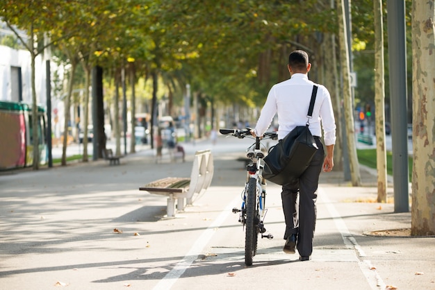 Vista trasera del hombre de negocios caminando con la bicicleta en el parque